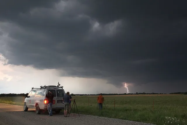 This may contain: people standing in the back of a van on a dirt road under a dark sky