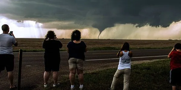 This may contain: several people standing on the side of a road watching a storm