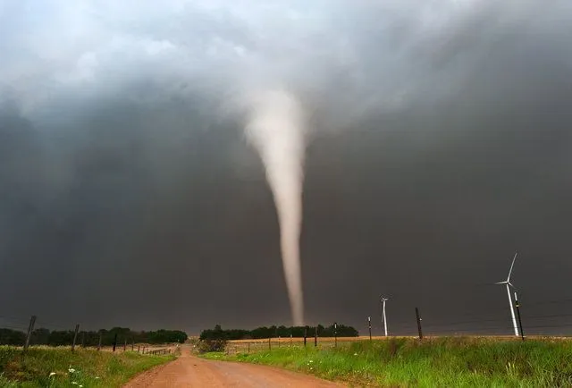 This may contain: a tornado is coming out of the sky over a dirt road