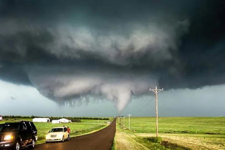 This may contain: two cars driving down a road under a large tornado