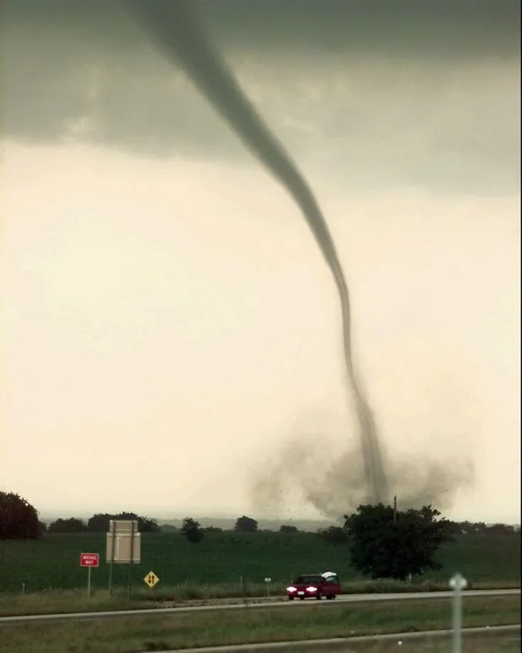 This may contain: a large tornado is seen in the sky over a highway