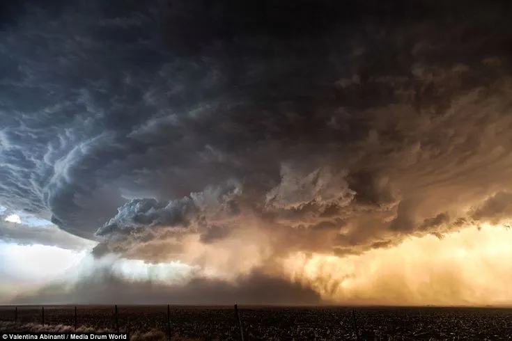 This may contain: a large storm cloud looms over an open field