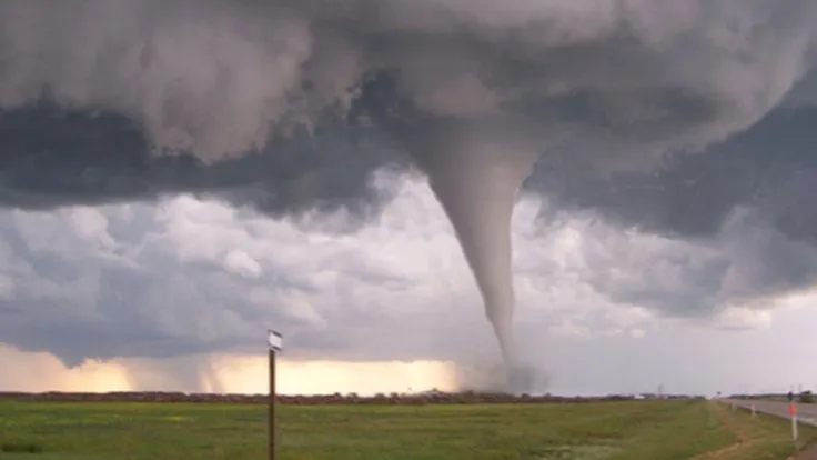 This may contain: a large tornado is seen in the sky over a road and grassy field with traffic signs