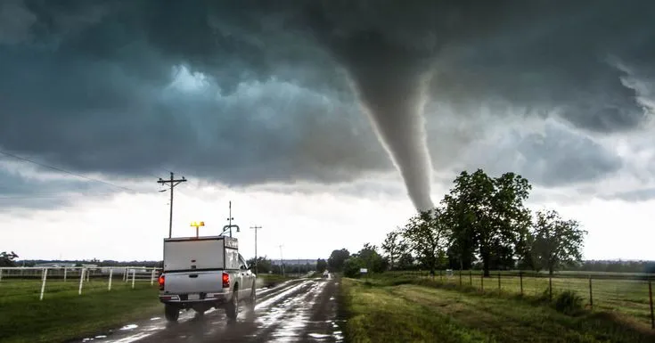 This may contain: a truck driving down a road under a large tornado
