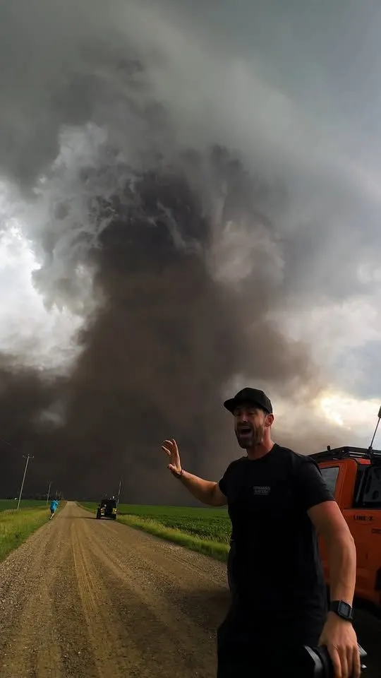 This may contain: a man is standing in the middle of a dirt road with an approaching storm behind him