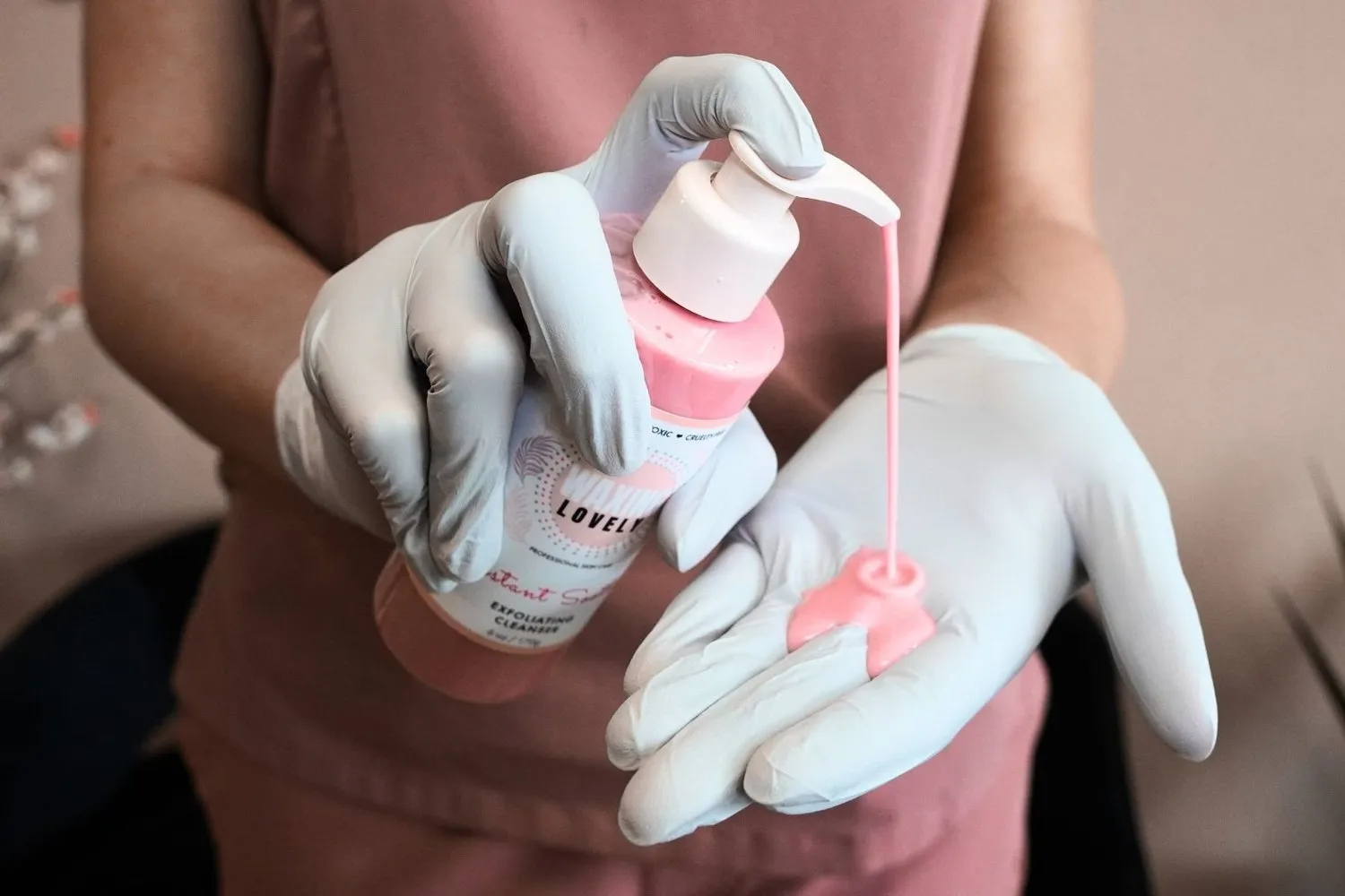 Esthetician pumping lotion on her hand while wearing gloves