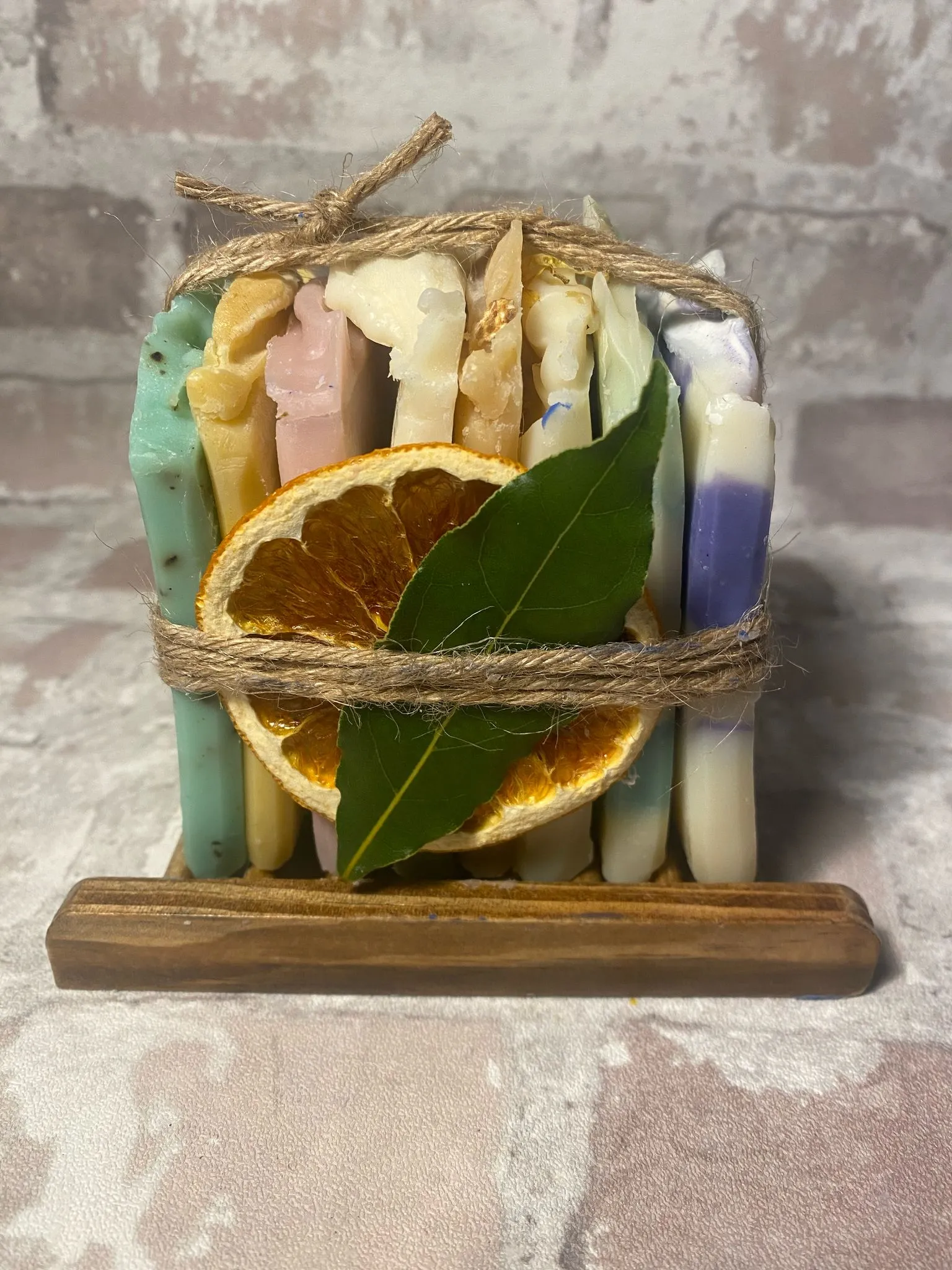 A variety of sample soap slabs tied together with natural twine, presented on a bamboo soap rack, with dried orange and leaf.