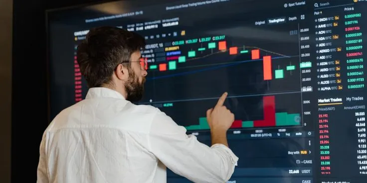 This may contain: a man points at a screen displaying stock prices on it, while pointing to the bar chart