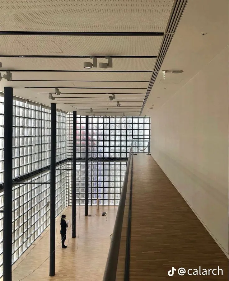This may contain: an empty room with lots of glass blocks on the wall and people walking in it