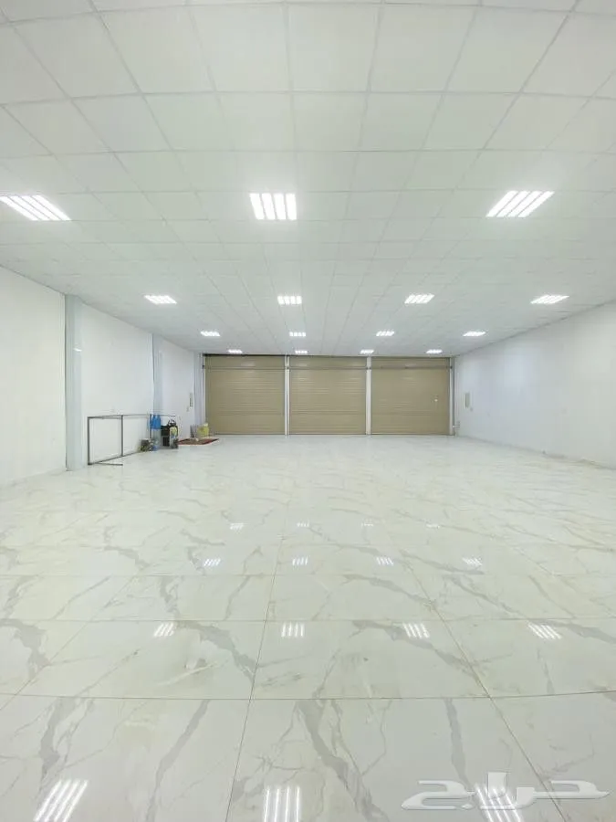 This may contain: an empty warehouse with white marble floors and lights on either side of the door that leads to another room