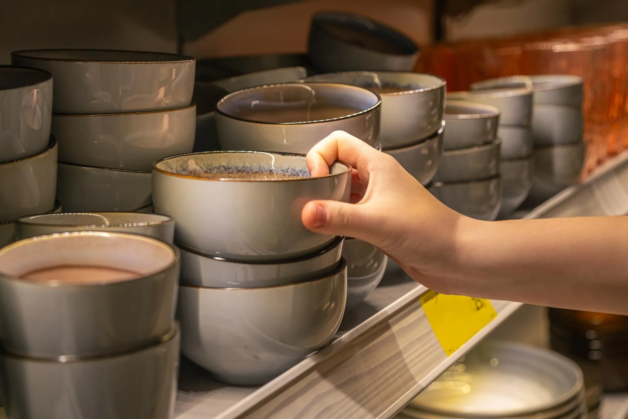 female hand holding bowl from a shelf in homeware store