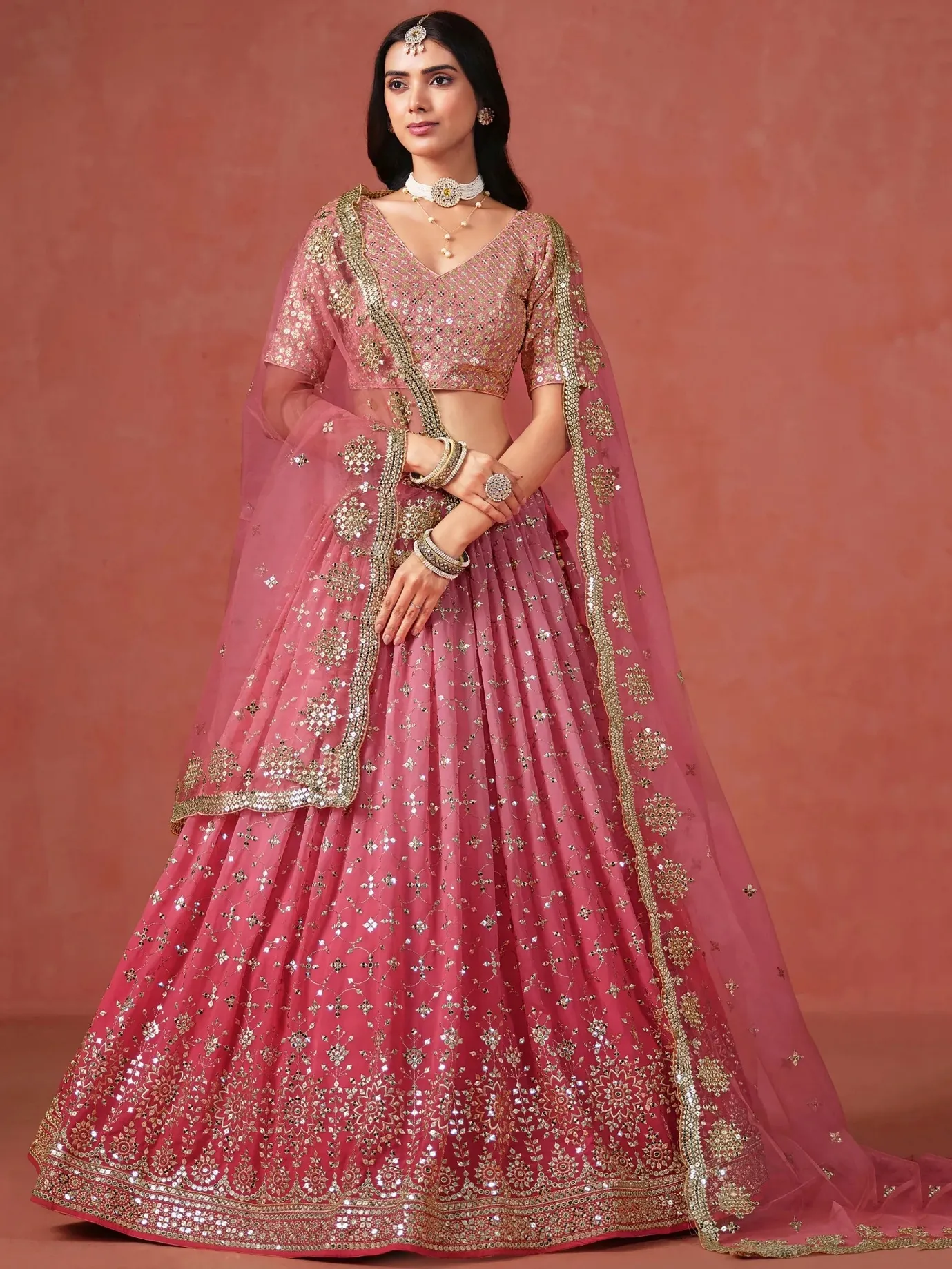 Woman wearing a pink designer lehenga choli with heavy mirror work and matching dupatta