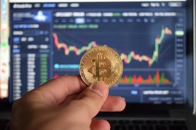 This may contain: a person holding a bit coin in front of a laptop