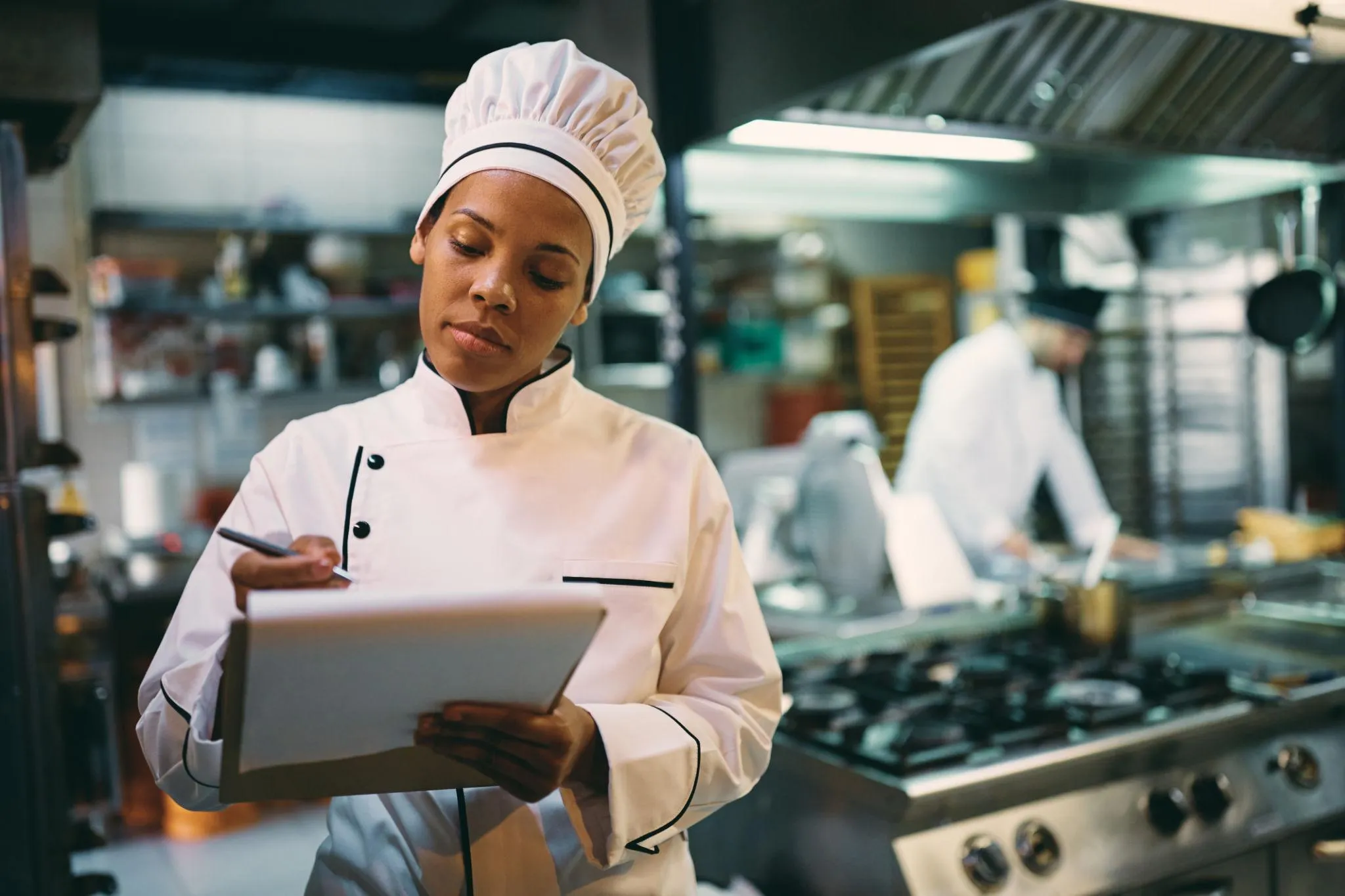 Black female chef going through checklist while working in the kitchen at restaurant.