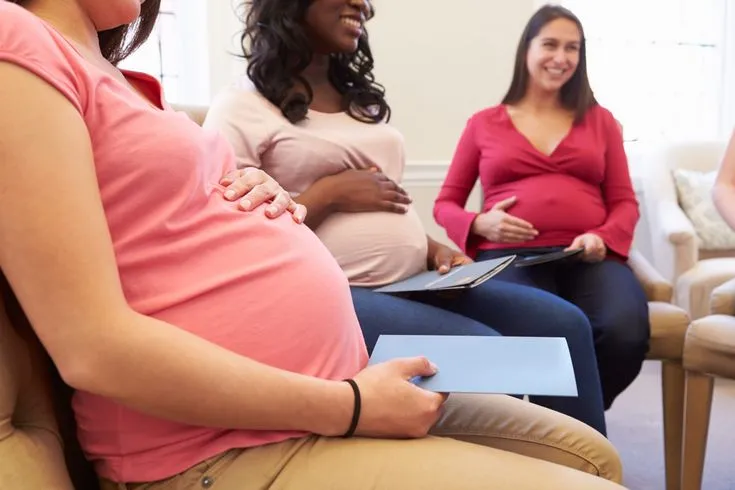 This may contain: three pregnant women sitting on couches in a living room, one holding a folder